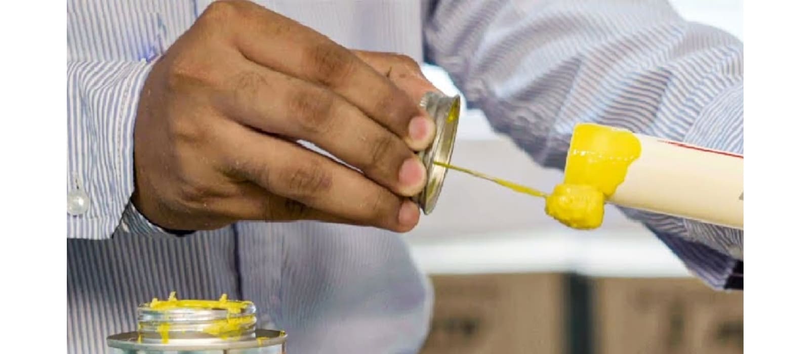 A plumber tipping yellow PVC solvent from its tin onto the end of a white PVC pipe