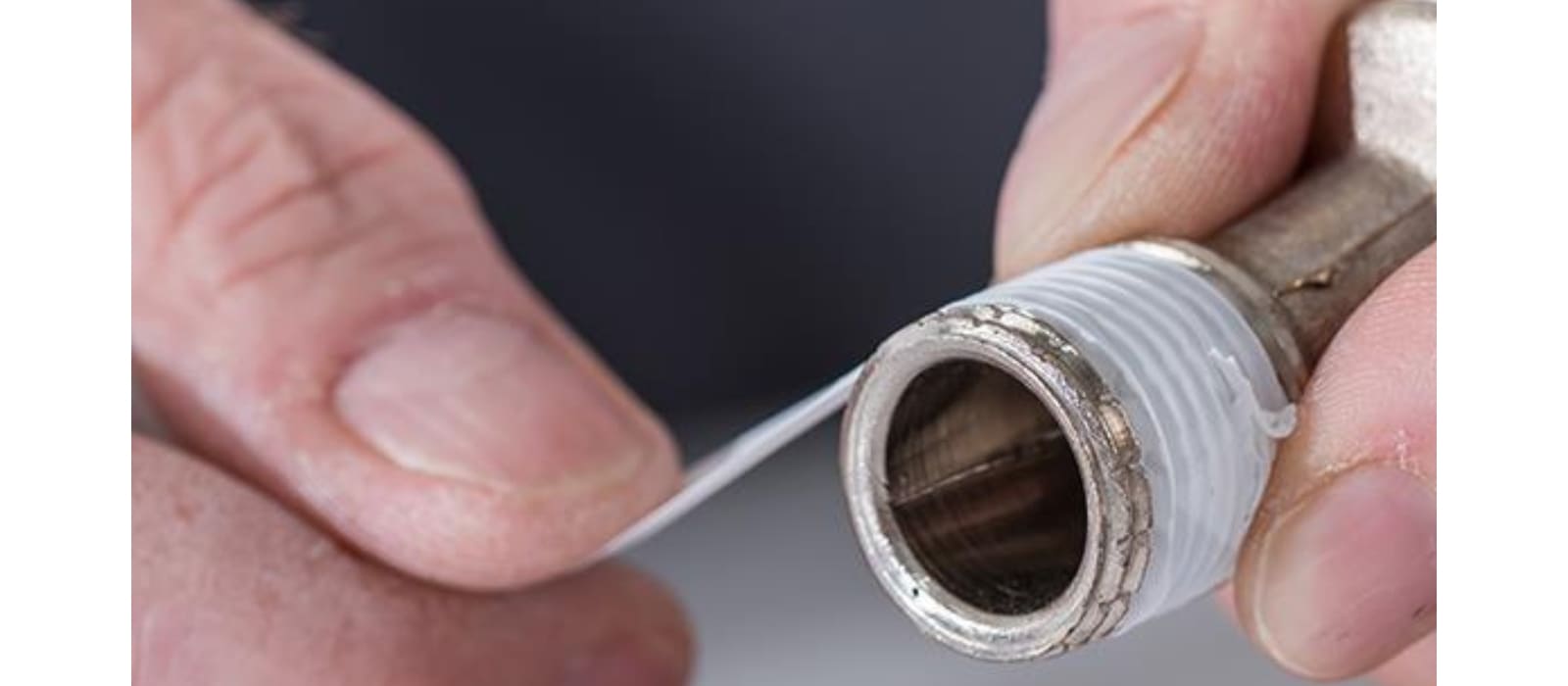Hands winding white Teflon tape around the threads of a metal pipe fitting